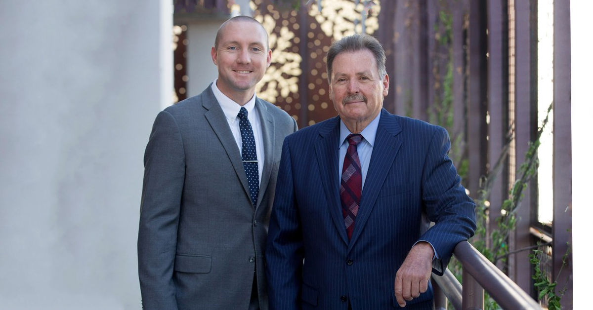 Two professional male attorneys in suits standing together outside a law firm building
